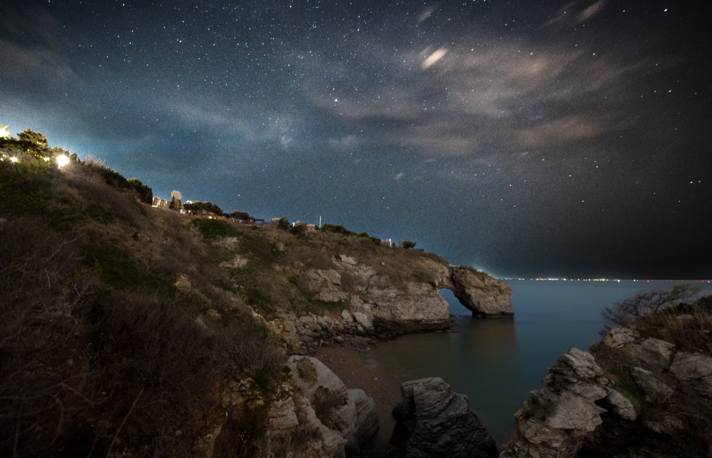 Stars over a coastal rock arch and still water at night
